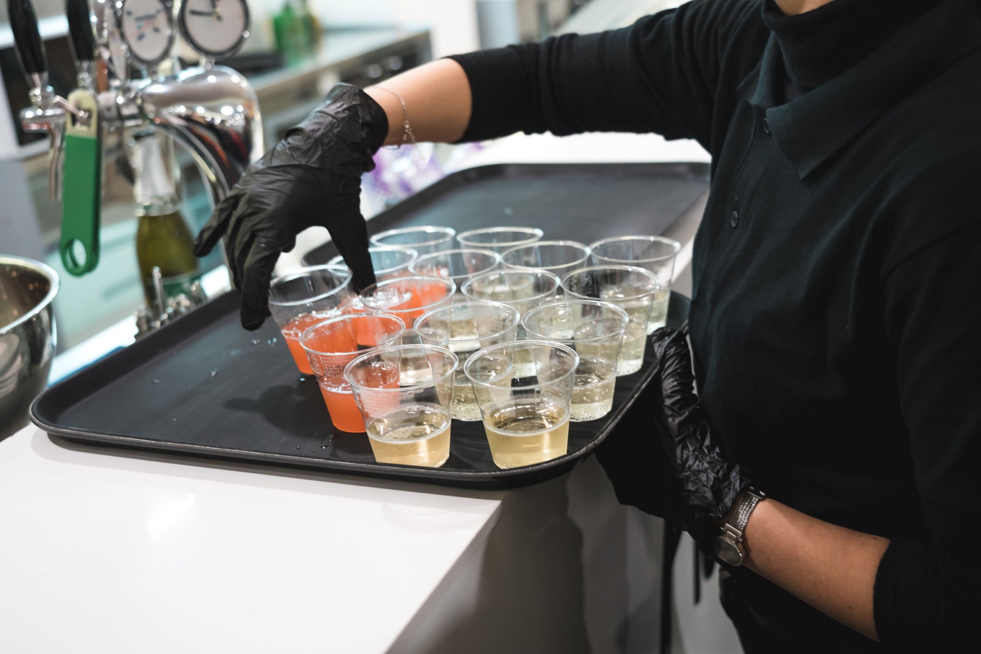 Unrecognizable waitress with black gloves preparing alcoholic drinks on a tray